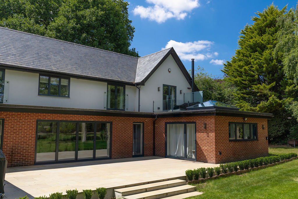 Two-storey rear house extension with brick finish, large sliding glass doors and modern patio leading to a landscaped garden.