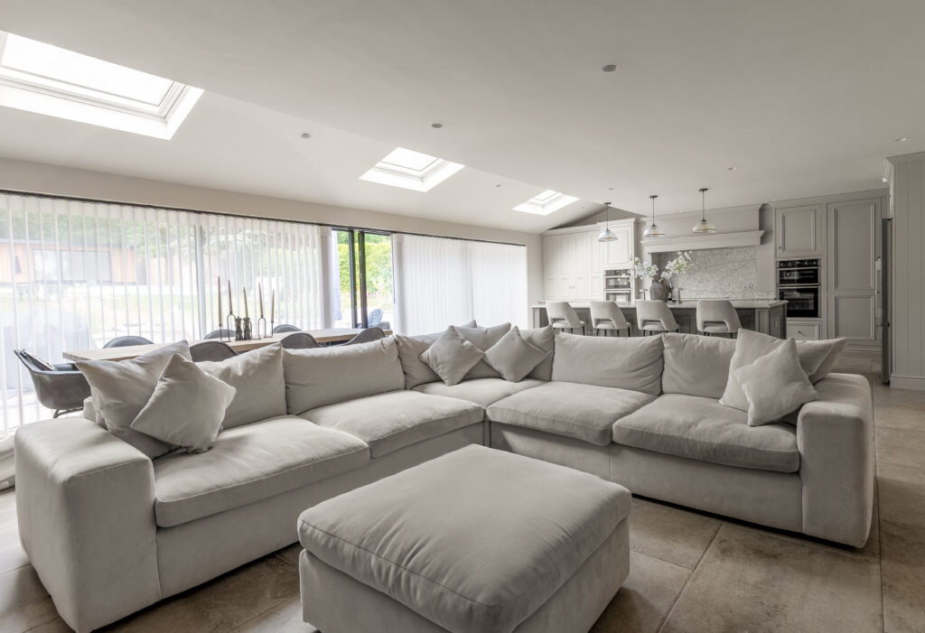 Open-plan rear extension living space with large corner sofa, skylights and modern kitchen with island and bi-fold doors to the garden.