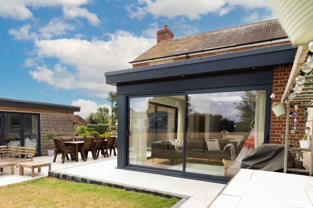 Modern rear house extension with large sliding glass doors opening onto a patio garden with outdoor seating and dining area.